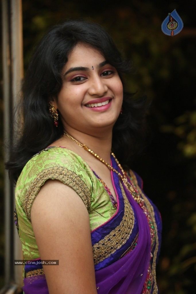 Krishnaveni smiling with black wavy hair and bindi on her forehead  while wearing earrings, necklace, and a colorful saree