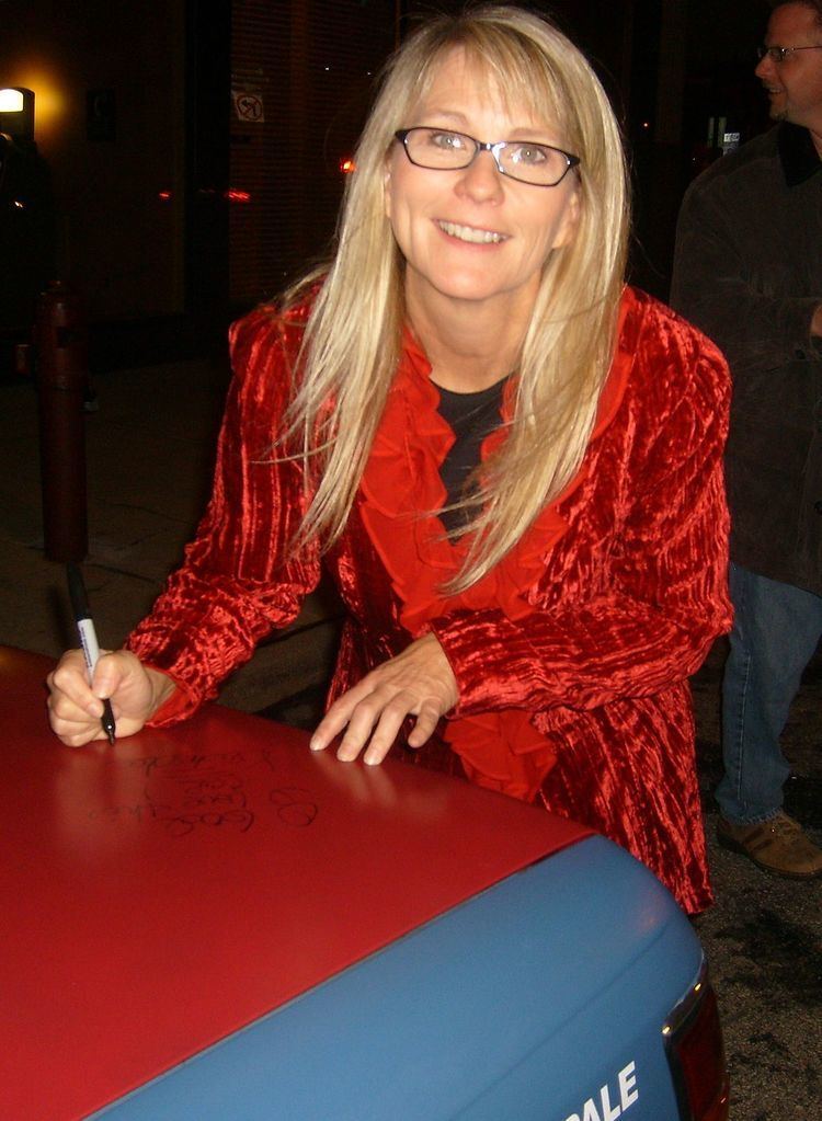 Kristi Lee smiles while holding a marker wearing a red long sleeve and eyeglasses
