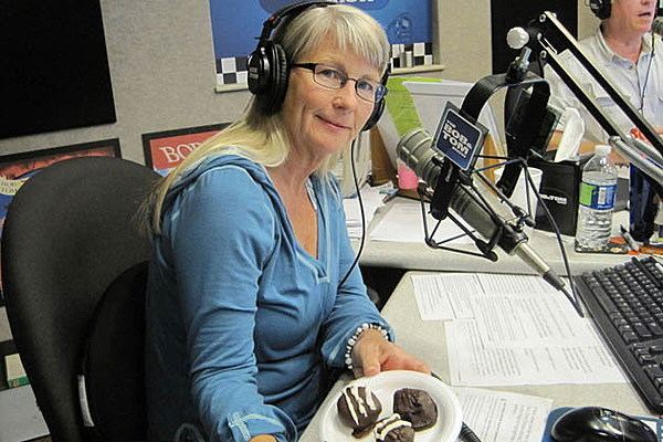 Kristi Lee sitting on a chair wearing blue long sleeves, eyeglasses, and headphones in the radio station