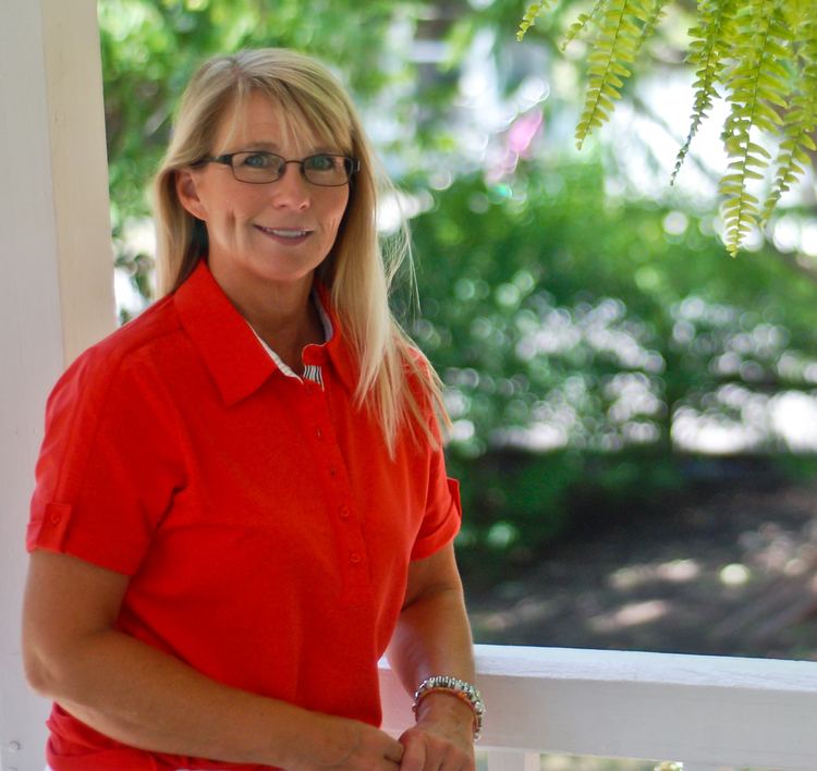 Kristi Lee smiles while wearing a red shirt and eyeglasses outdoor