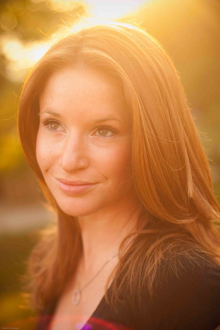 Kristin Fisher smiling, with blonde hair and wearing a necklace and a black shirt.