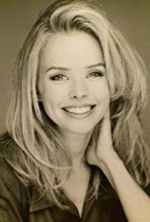 Kristina Wagner is smiling, has wavy blonde hair, wearing a black collared top, her right hand on her neck.