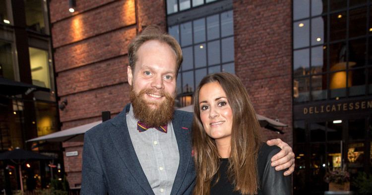 Kristine Riisand and Jon Niklas Ronning smiling, Kristine with long blonde hair and wearing a black dress while Niklas with beard and mustache, wearing a bow tie, a blue coat over gray long sleeves.