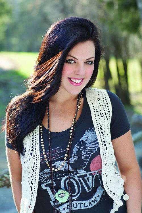 Krystal Keith smiling while wearing a black printed shirt, white vest, and necklace