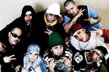Seven members of Kumbia Kings posing with hand gestures and wearing street gang themed clothing.