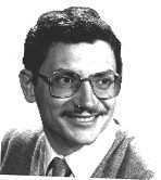 Kurt Wise smiling with mustache and wearing eyeglasses, a shirt under a coat and necktie