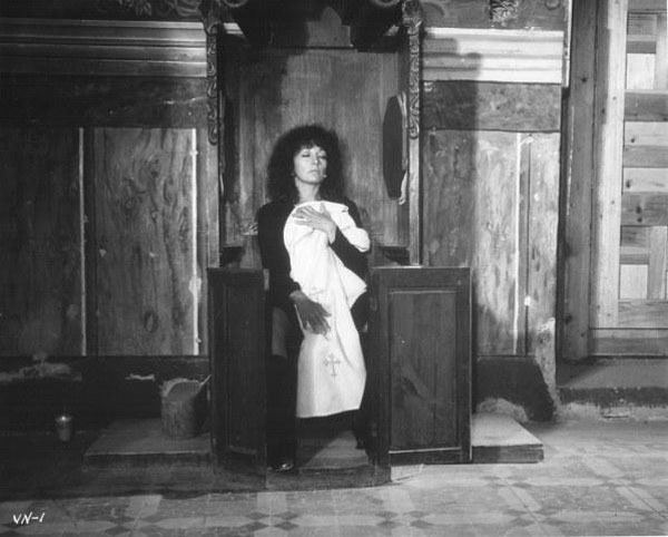 Isela Vega as Matea kneeling inside a church and holding a white priest outfit and wearing a black dress in a scene from La Viuda Negra, 1977.