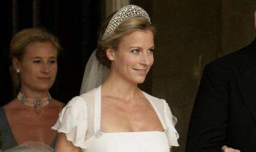 Lady Rose Gilman with a tight-lipped smile while wearing a wedding gown, crown, and veil