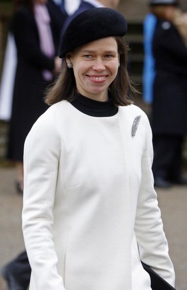 Lady Sarah Chatto is smiling, has black hair, wearing a black hat, silver earrings, and a black and white top with a leaf pin on her right chest.