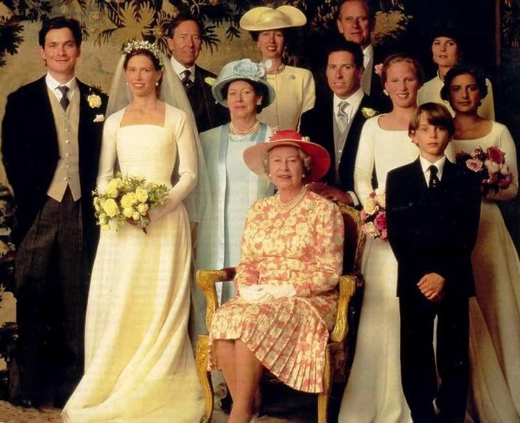 Daniel Chatto (left) is smiling, has black hair, wearing white long sleeves, a black necktie, an off-white vest under a black suit with a flower on his left pocket, black pants, and black shoes. 2nd from the left is Lady Sarah Armstrong-Jones smiling, has black hair, wearing white earrings, a veil with tiara, a long gown, and both hands holding a bouquet of flowers. 3rd from left is Princess Margaret the mother of Lady Sarah Armstrong-Jones, smiling, has black hair, wearing silver earrings and a necklace, a blue hat with a blue flower, and a blue dress under a blue coat. 4th from left is Queen Elizabeth, sitting down on a brown chair, smiling, both hands on her lap, has blonde hair, wearing silver earrings and a necklace, a red hat, white gloves, and a red floral dress. Together with the Royal Family in the background wearing suits and gowns.