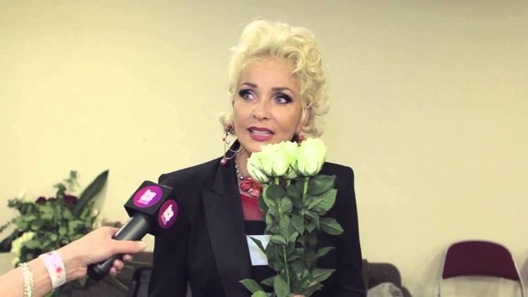 Laima Vaikule speaking during an interview and holding white roses while wearing a black coat