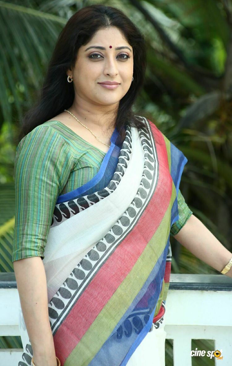 Lakshmi Gopalaswamy wearing a colorful dress and jewelries while trees on her background