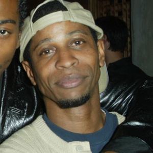 Larry B. Scott smiles while wearing a white and blue shirt, and a hat