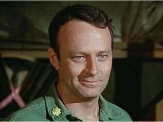Larry Linville smiling while wearing a green shirt in a scene from the TV series MASH