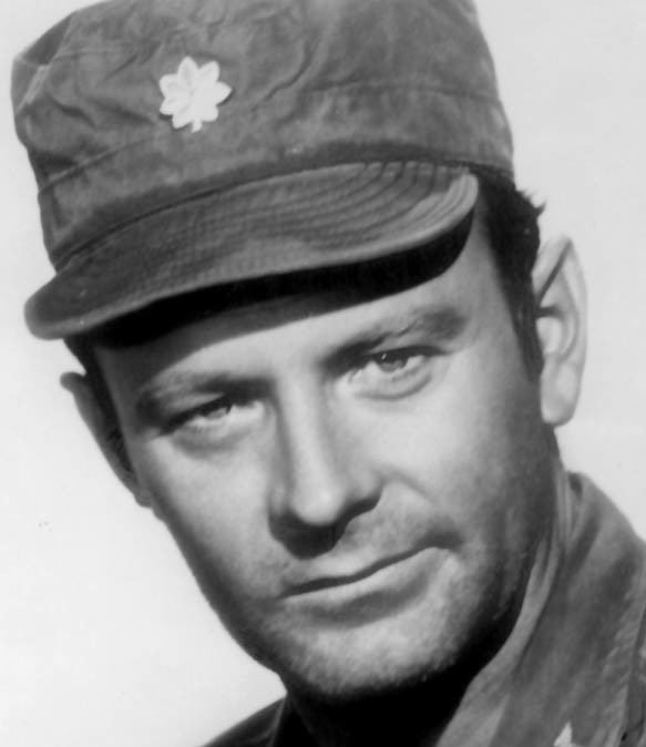 Larry Linville smiling and wearing a cap