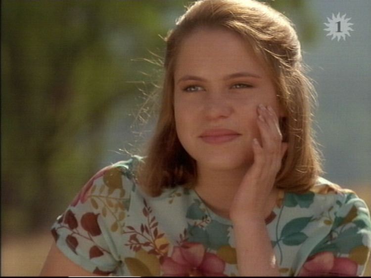 Lauren Hewett smiling with her left hand on the cheek and looking at something while wearing a floral blouse