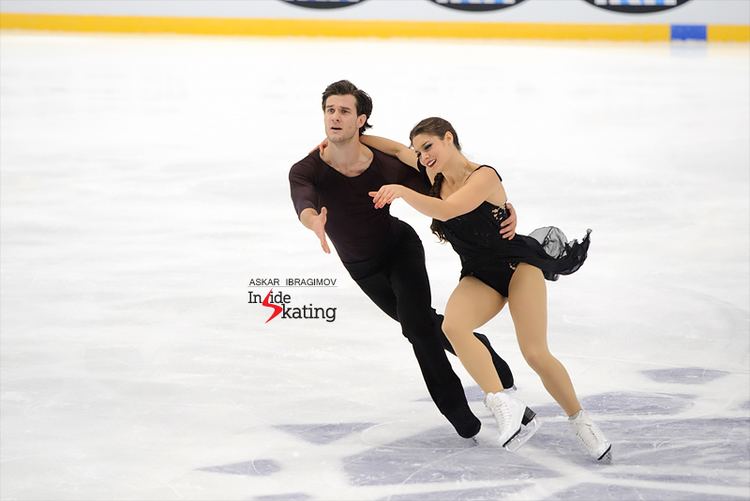 Laurence Fournier Beaudry holding performing a dance on the ice rink with Nikolaj Sorensen. Laurence wearing a black short dress and white figure skate while Nikolaj wearing a black long sleeve, black pants, and black figure skate