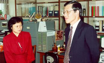 Lee Yock Suan wearing eyeglasses, a suit, and a striped tie with a woman wearing a red dress.