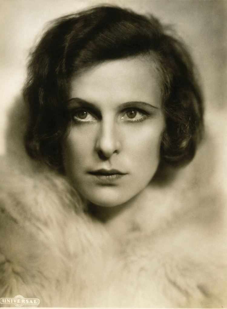 Leni Riefenstahl with a serious face, short wavy hair, and wearing a fur coat.