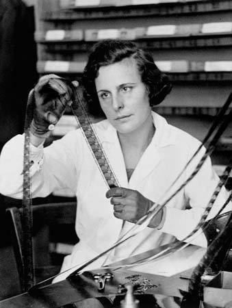 Leni Riefenstahl wearing white long sleeves with a serious face while looking at a camera film.