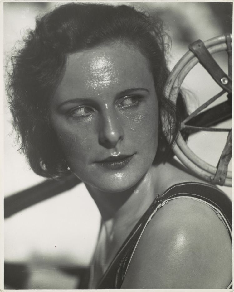 Leni Riefenstahl with a serious and shiny face and wearing a sleeveless top.