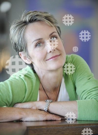 Lenore Smith smiling while leaning on the table and wearing a white blouse and green cardigan