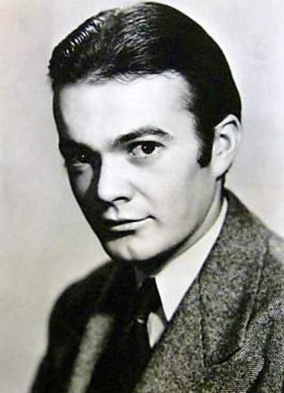 Leo Gorcey with a serious face, wearing a gray coat over white long sleeves, and a black necktie.