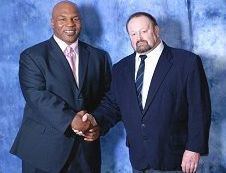 Lew Yates shaking hands with the man beside him while he is wearing white long sleeves, blue striped necktie, and dark blue coat