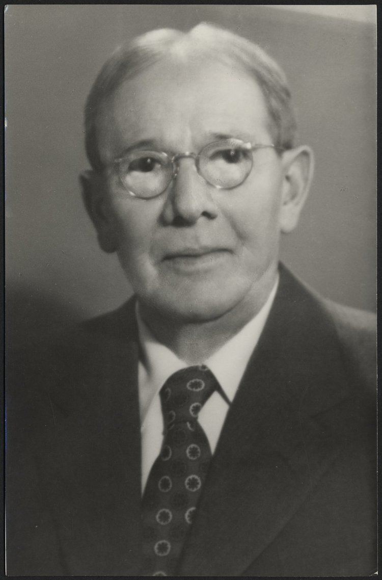 Lewis Terman with a serious face while wearing eyeglasses and a black suit with a tie