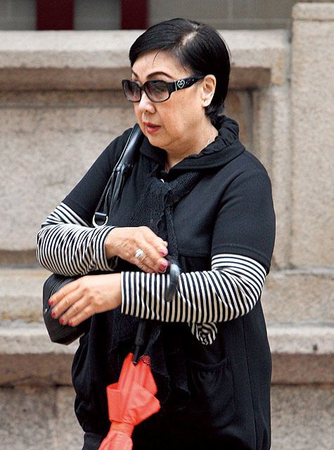 Li Ching holding an orange umbrella while carrying a black bag and wearing a black and white long sleeve blouse and black sunglasses