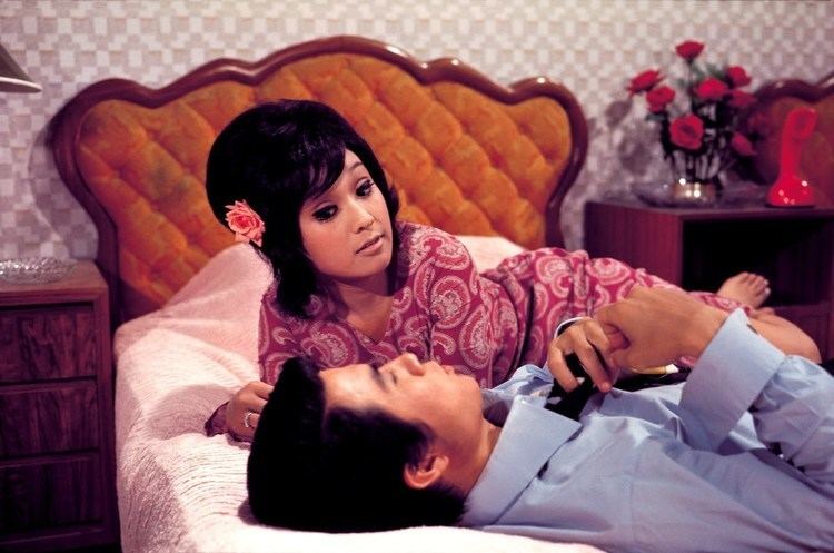 Li Ching lying on the bed while looking at the man beside her and she is wearing a red dress in a scene from the 1972 film, The Merry Wife