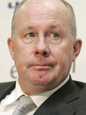 Liam Brady with a serious face and wearing a black suit and a tie.