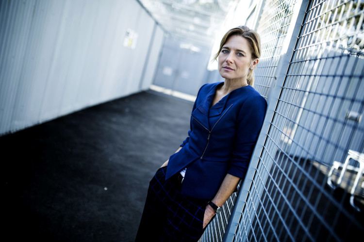 Libby Tanner wearing a blue suit, checkered blue jeans, and a watch.