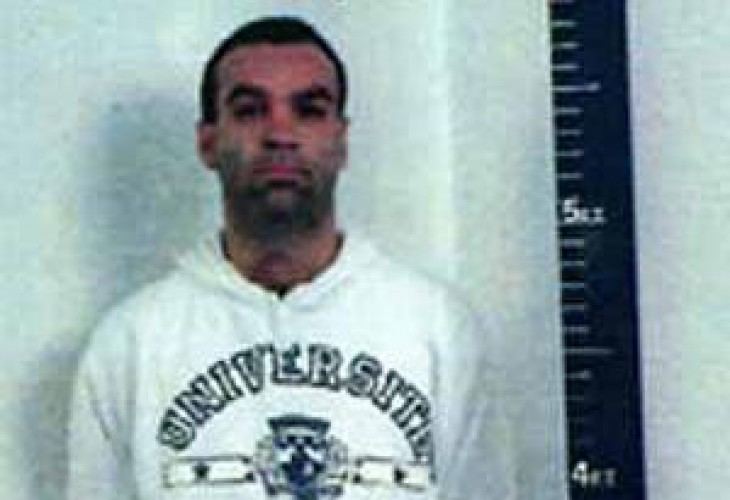 Liborio Bellomo is serious, has black hair, a beard, and a mustache, both hands on his back, and a height measurement on right, and wears a white hoodie jacket with the print "UNIVERSITY" at the center.