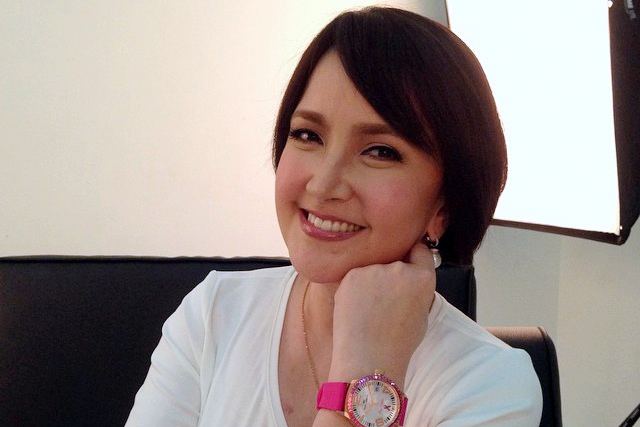 Liezl Martinez is smiling, has black short hair, wearing pearl earrings, a gold necklace, a pink wristwatch on her left hand, and a white top.