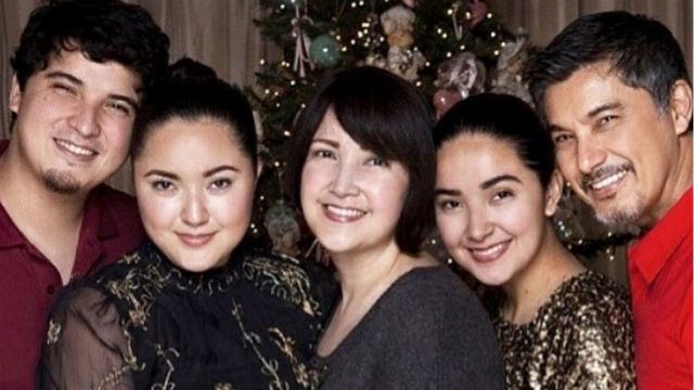 Alfonso Martinez (left) is smiling, has black hair and a mustache, wearing a maroon shirt. 2nd from the left is Alyanna Martinez, she is smiling, has black hair, wearing a black dress with a design. In the center is Liezl Martinez smiling, has black short hair, standing in front of the Christmas tree, and wearing a black top. 4th from left is Alissa Martinez smiling, has black hair, and wearing a black shimmering top. On right is Albert Martinez smiling, has black and white hair, a beard and mustache, and wearing a red shirt.