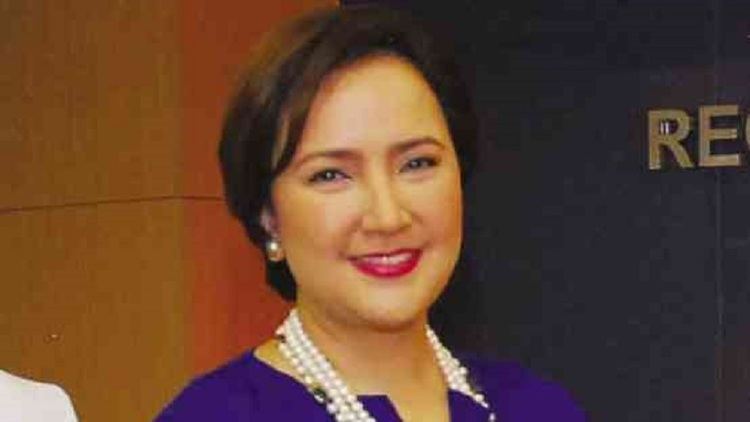 Liezl Martinez is smiling, has black short hair, wearing pearl earrings, a necklace, and a violet top.