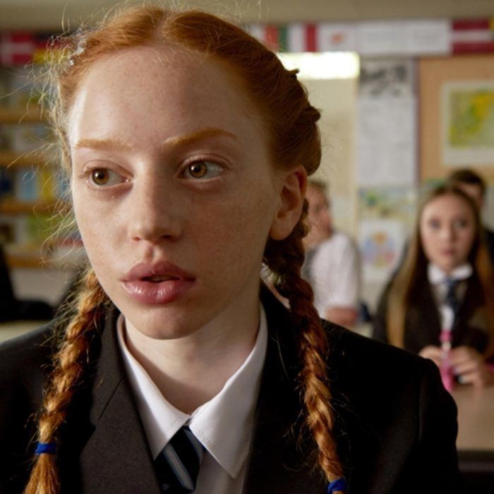 Lily Newmark with braided hair while wearing a black coat, white blouse, and striped necktie in a scene from the 2017 film, Pin Cushion