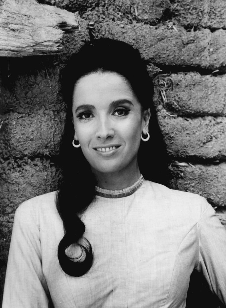 Linda Cristal smiling while wearing a long sleeve dress and earrings