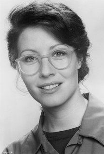 Linda Kozlowski smiling, wearing eyeglasses and a coat over a black shirt.