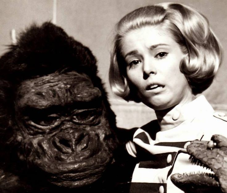 A scene from the movie "King Kong Escapes" featuring Linda Miller as 	Lieutenant Susan Watson with short blonde hair and with a frightened face and on her side is King Kong.