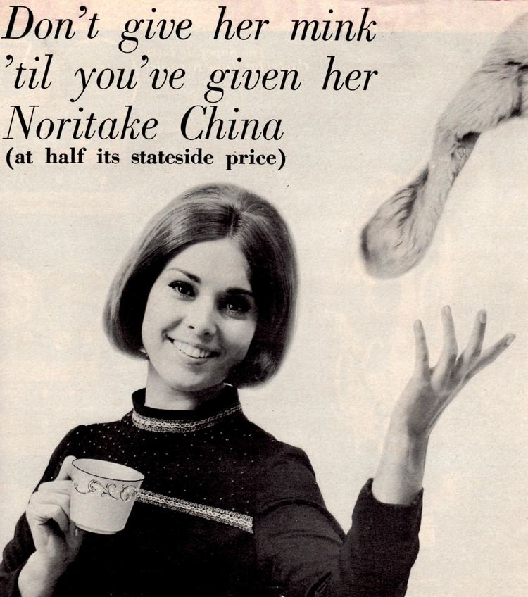 Linda Miller with short hair, wearing a black dress, and holding a cup.