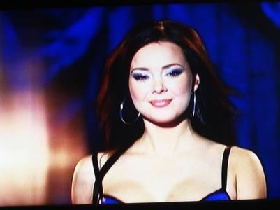 Lana Tailor as Vanessa smiling on stage and smiling closed mouth while wearing a dark blue lingerie and large earrings in a scene from Lingerie, 2009.
