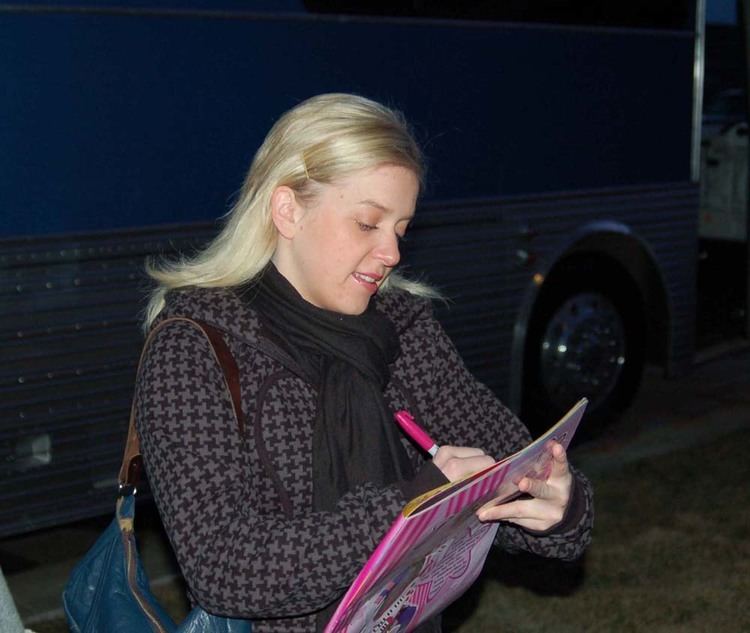 Lisa J. Lennox writing outside wearing a jacket, a scarf, and a bag