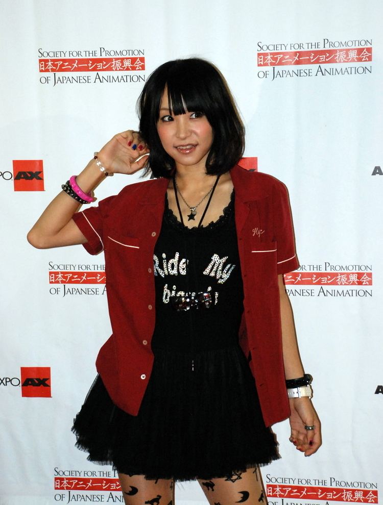 LiSA smiling while wearing a red blazer, black inner top, and black skirt