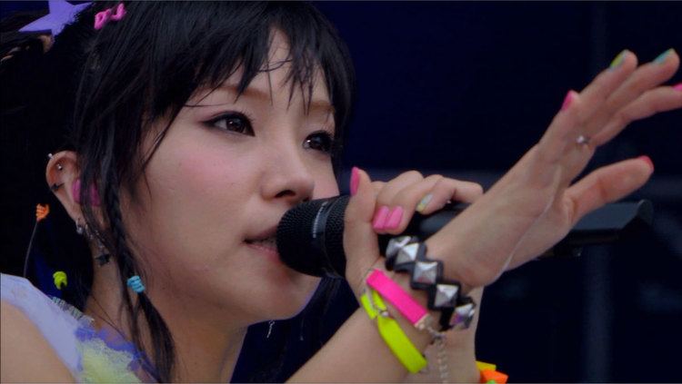 LiSA holding a microphone and wearing colorful bracelets and hair clips