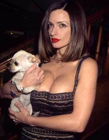 Lisa Marie carrying a dog while wearing a brown and black sleeveless blouse showing off her cleavage