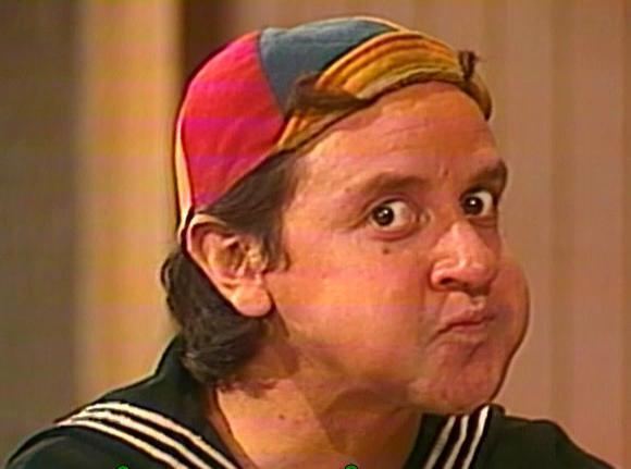 Carlos Villagrán as Quico wearing a cap and black and white polo