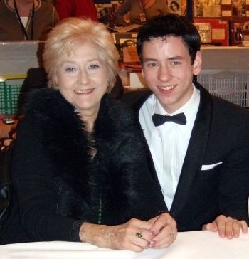 Liz Fraser smiling and wearing a black furry coat with Ciaran Brown with a smiling face and wearing a black suit, white long sleeves, and black bow tie.