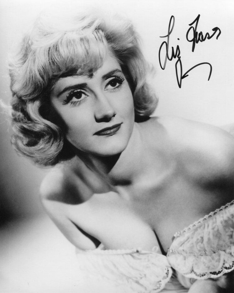 Liz Fraser with curly blonde hair and wearing a sexy top showing her cleavage.